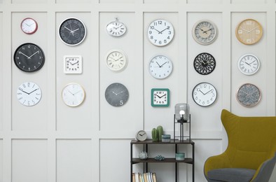 Photo of Armchair, console table and many different clocks hanging on white wall in room