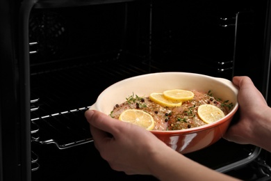 Woman putting chicken breasts with lemon and rosemary into oven, closeup