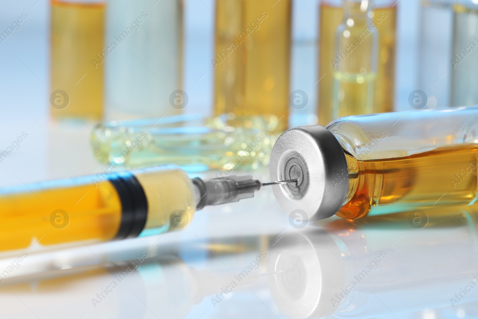 Photo of Filling syringe with orange medication from glass vial on white table, closeup