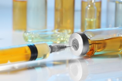 Photo of Filling syringe with orange medication from glass vial on white table, closeup