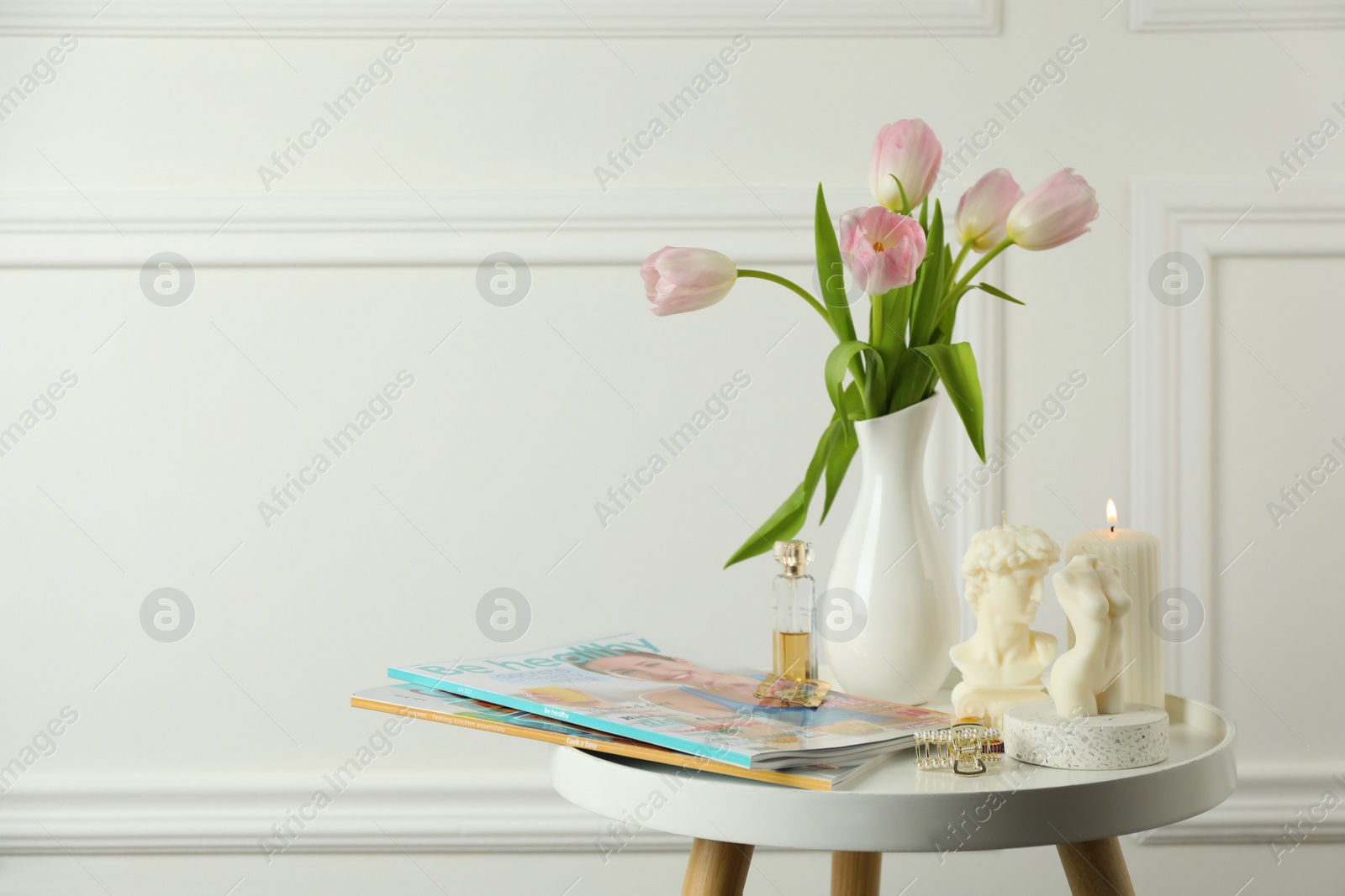 Photo of Different beautiful candles and tulips on white table, space for text. Stylish decor