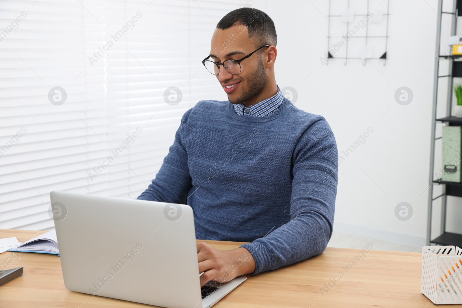 Photo of Happy young intern working with laptop at table in modern office