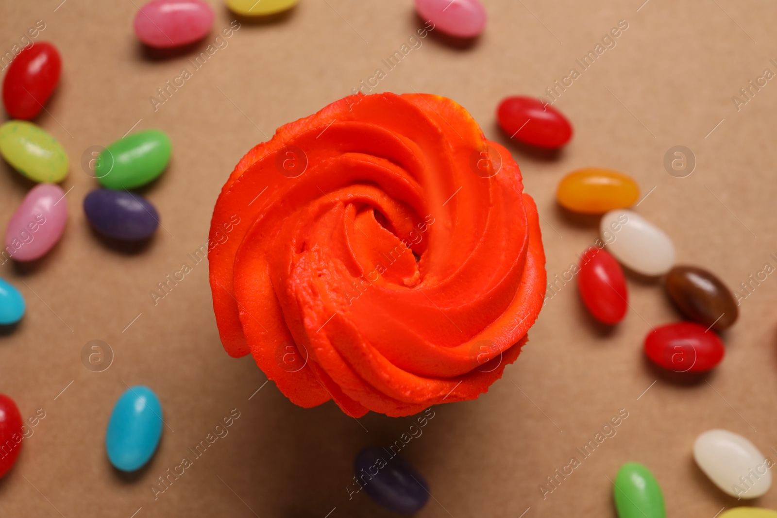 Photo of Delicious cupcakes with bright cream and candies on brown background, flat lay