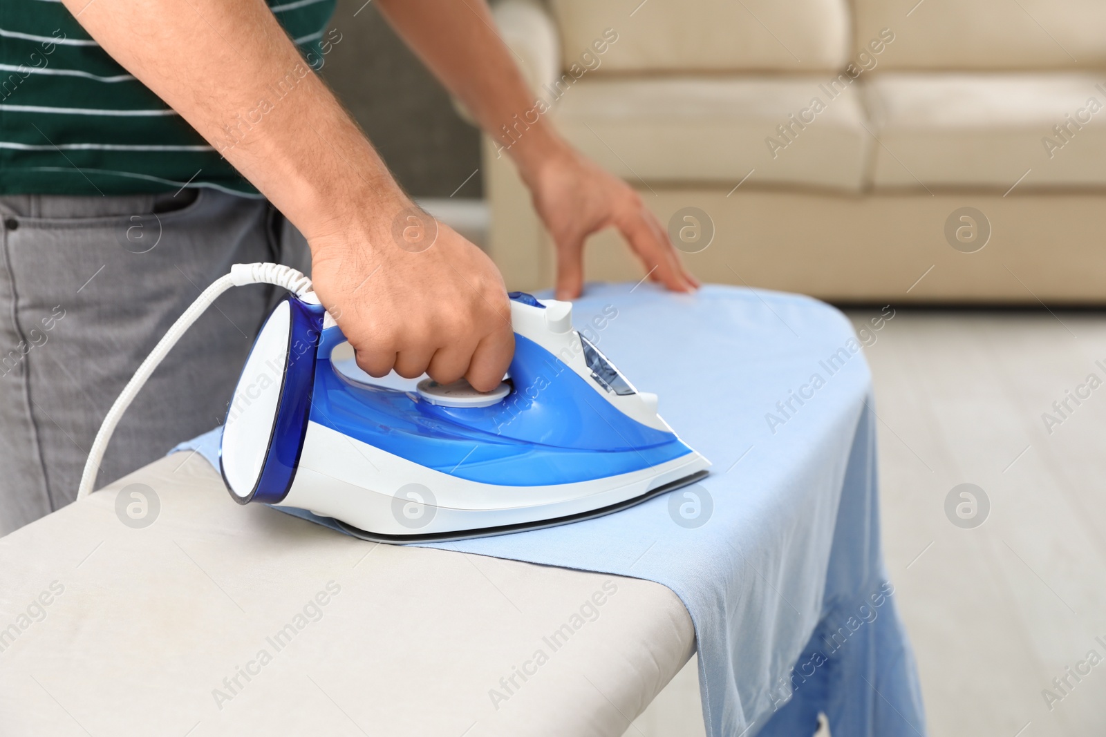 Photo of Man ironing shirt on board at home, closeup