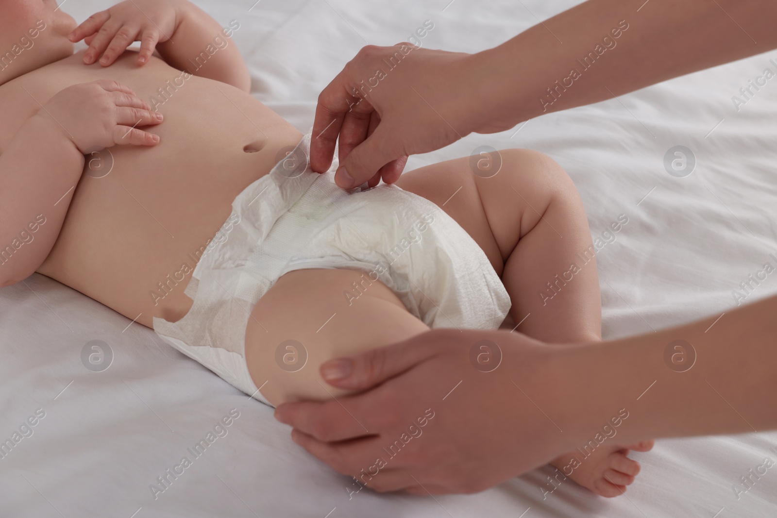 Photo of Mother changing her newborn baby's diaper on bed at home, closeup