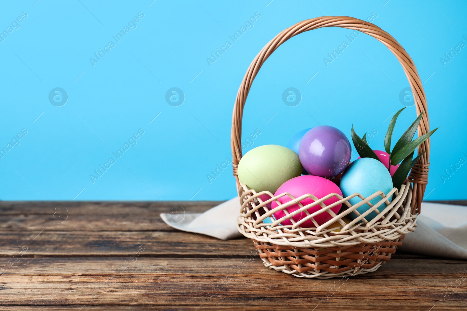 Photo of Colorful Easter eggs in wicker basket on wooden table. Space for text