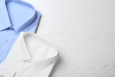 Photo of Stylish shirts on white wooden table, flat lay with space for text. Dry-cleaning service