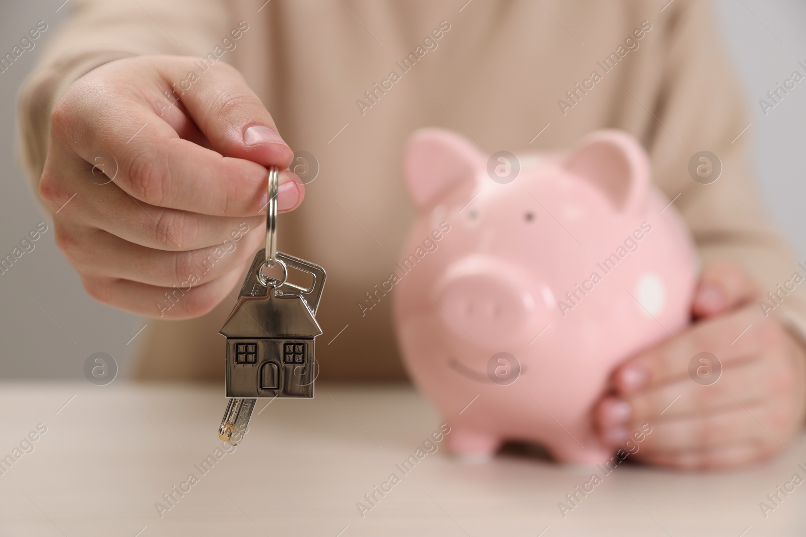 Photo of Man holding key and piggy bank at wooden table, closeup. Space for text. Saving money concept