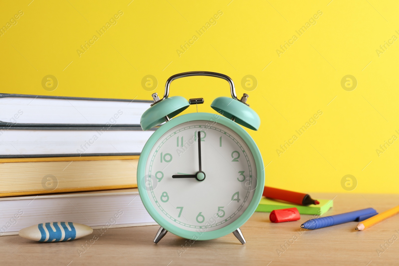 Photo of Turquoise alarm clock and different stationery on white wooden table against yellow background. School time