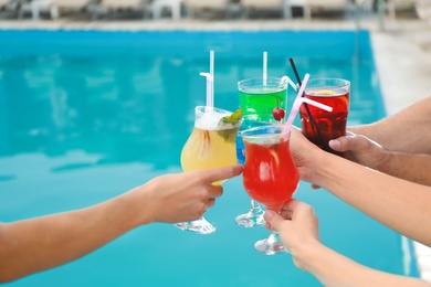 Friends clinking glasses with fresh summer cocktails near swimming pool, closeup