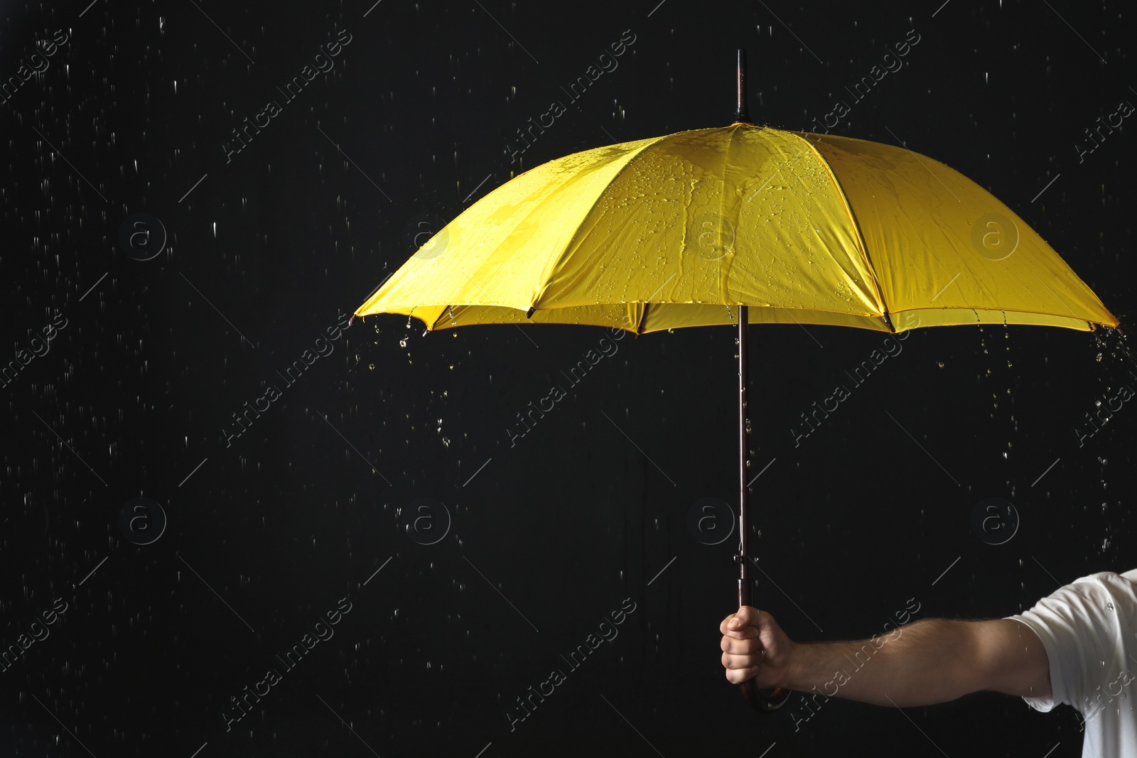 Photo of Man holding yellow umbrella under rain against black background, closeup