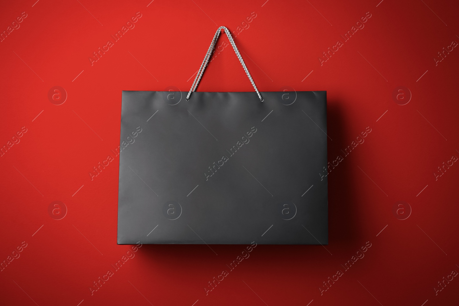 Photo of Paper shopping bag hanging on red background