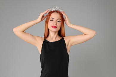 Beautiful young woman with tiara in dress on light grey background