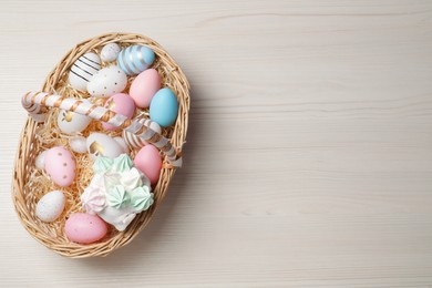 Photo of Easter basket with painted eggs and tasty cake on white wooden table, top view. Space for text