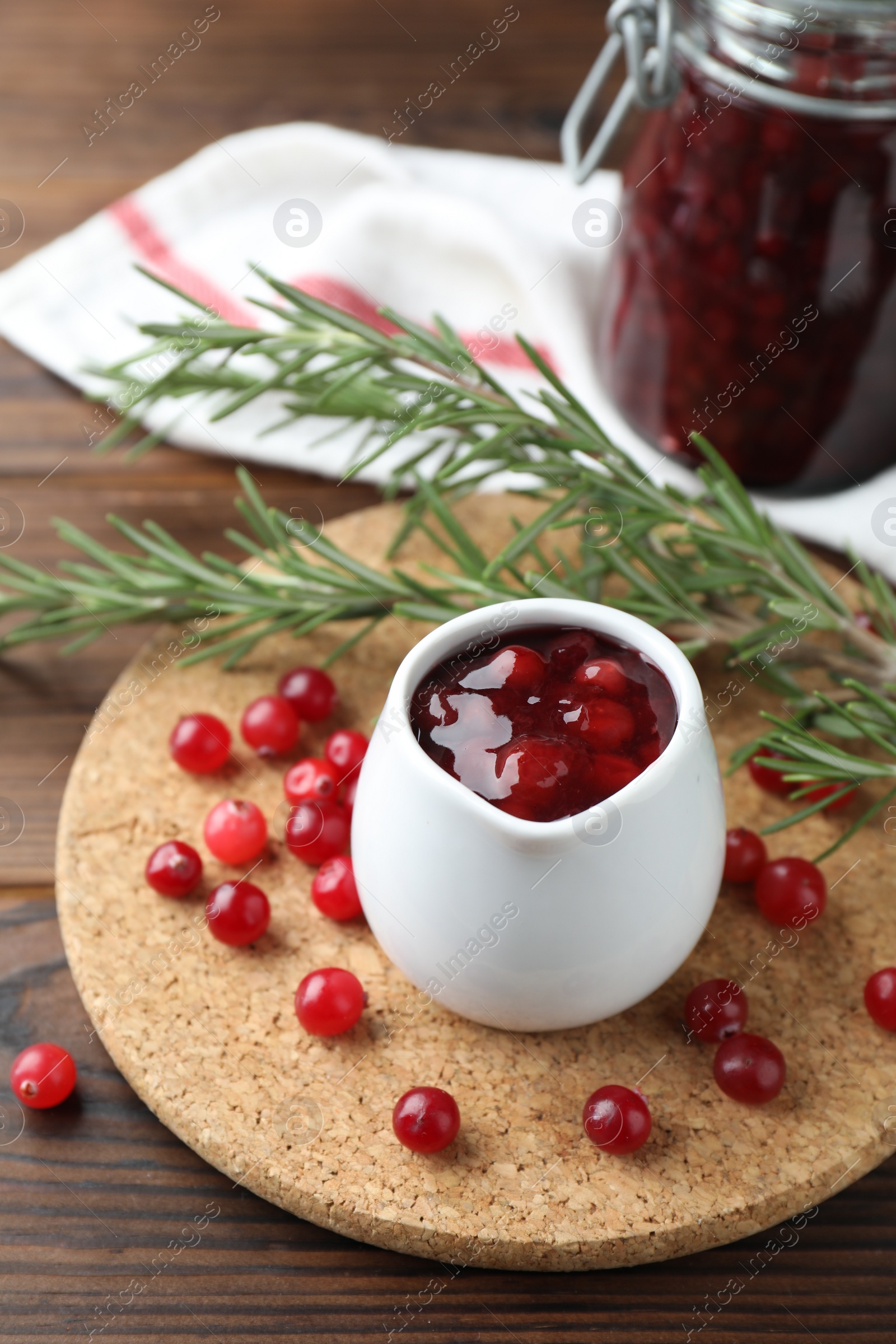 Photo of Cranberry sauce in pitcher, fresh berries and rosemary on wooden table