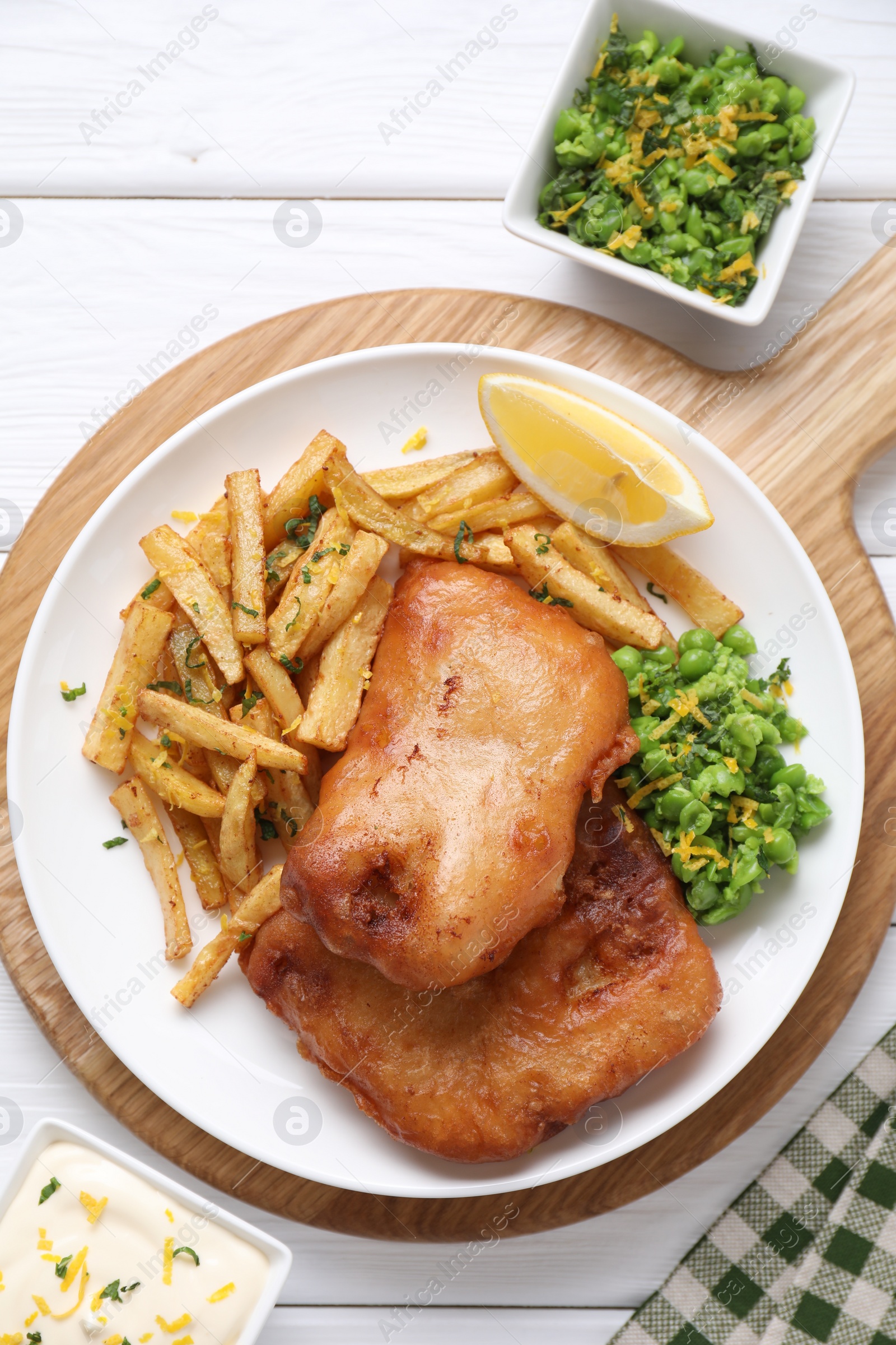 Photo of Tasty fish, chips, sauce, peas and lemon on white wooden table, top view