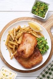 Photo of Tasty fish, chips, sauce, peas and lemon on white wooden table, top view