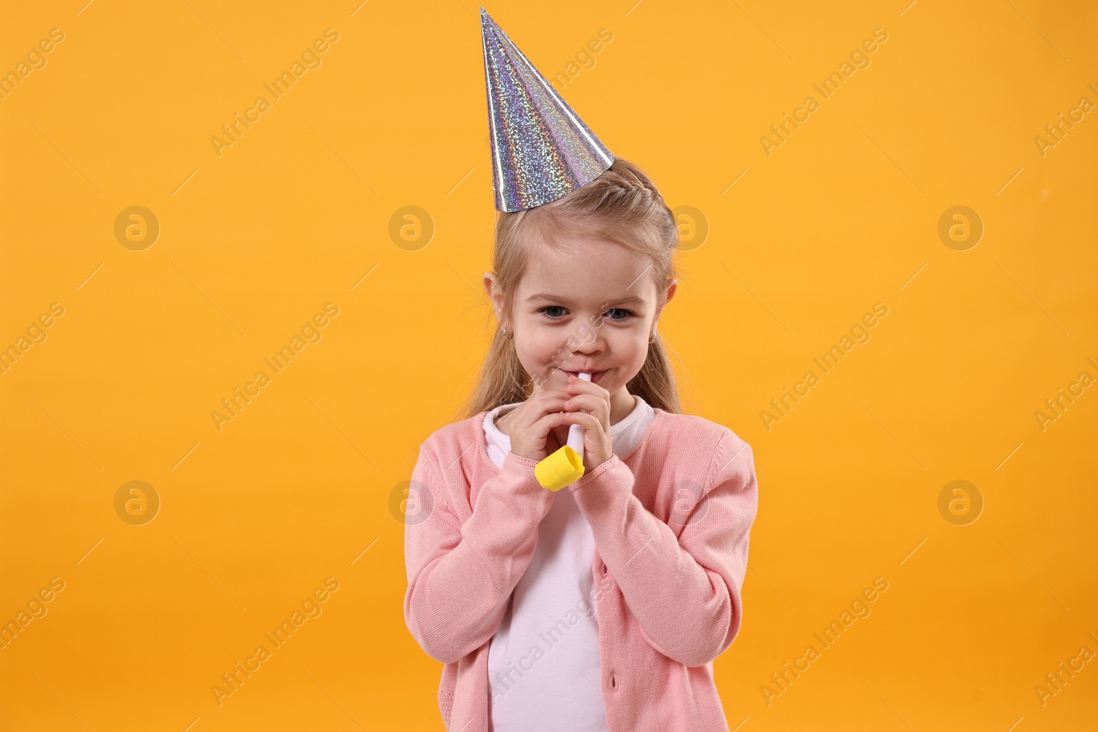 Photo of Birthday celebration. Cute little girl in party hat with blower on orange background