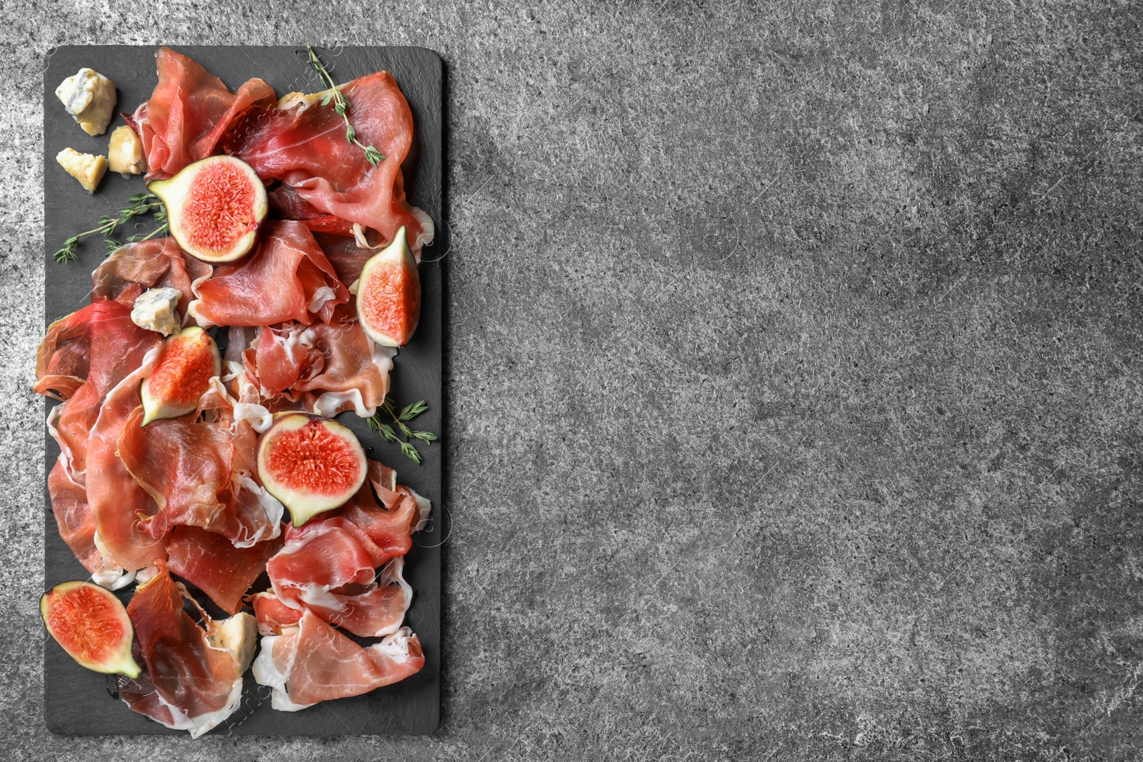 Photo of Delicious ripe figs and prosciutto served on grey table, flat lay. Space for text