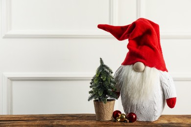 Cute Christmas gnome, small decorative fir tree and festive balls on wooden table. Space for text