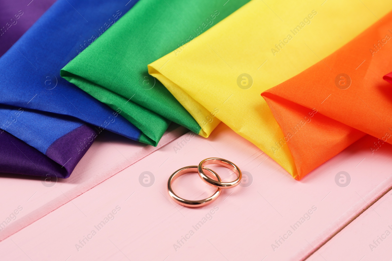 Photo of Rainbow LGBT flag and wedding rings on pink wooden table, closeup