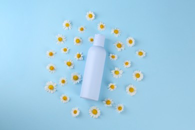 Bottle with skin care product for baby and daisies on light blue background, flat lay