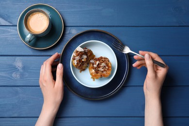 Woman eating delicious baked apple halves with nuts and caramel at blue wooden table, top view