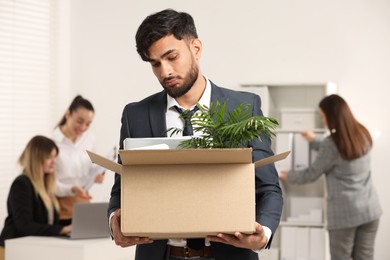 Photo of Unemployment problem. Frustrated man with box of personal belongings in office