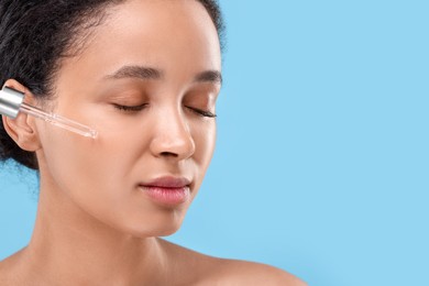 Beautiful woman applying serum onto her face on light blue background, closeup. Space for text