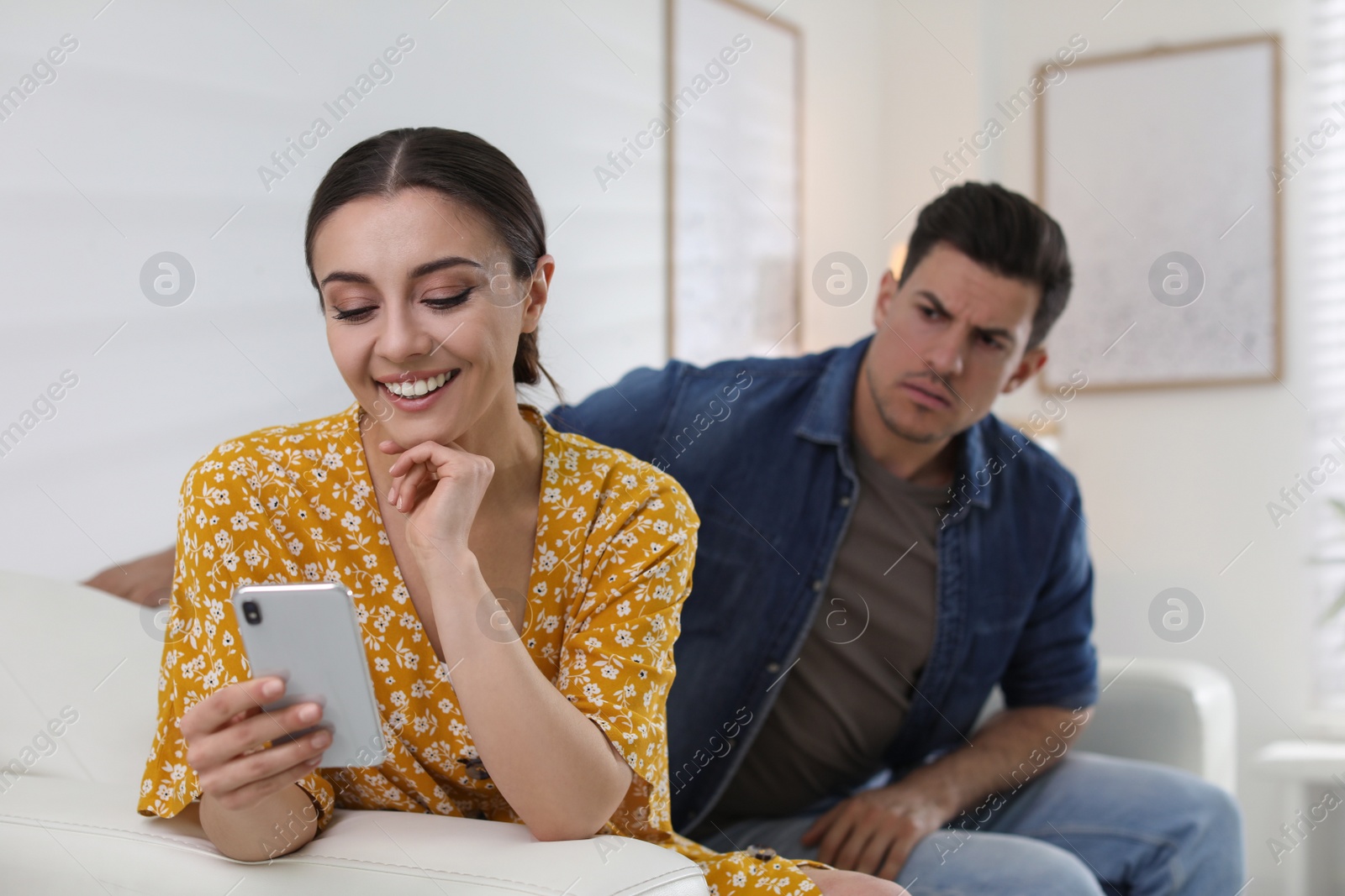 Photo of Distrustful man peering into girlfriend's smartphone at home. Jealousy in relationship