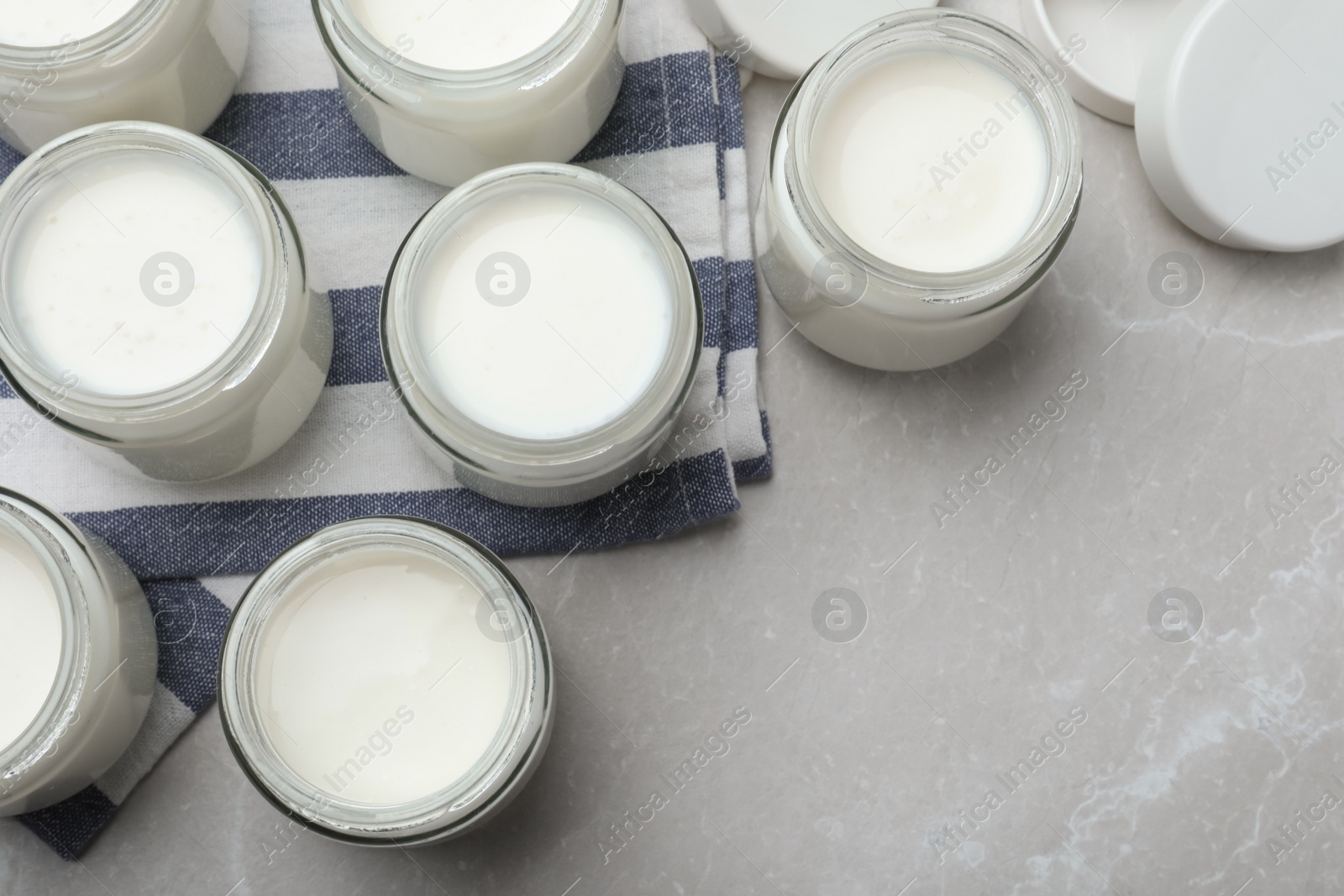 Photo of Tasty yogurt in glass jars on light grey marble table, flat lay