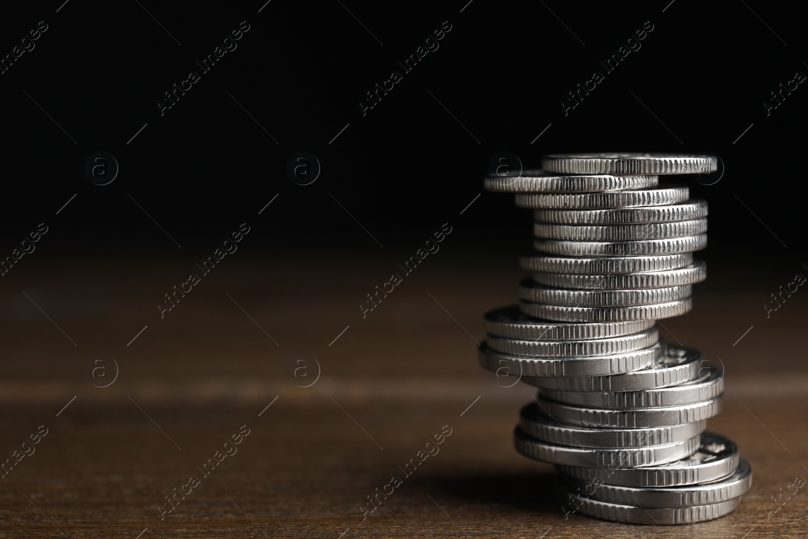 Photo of Many coins stacked on wooden table against black background, space for text