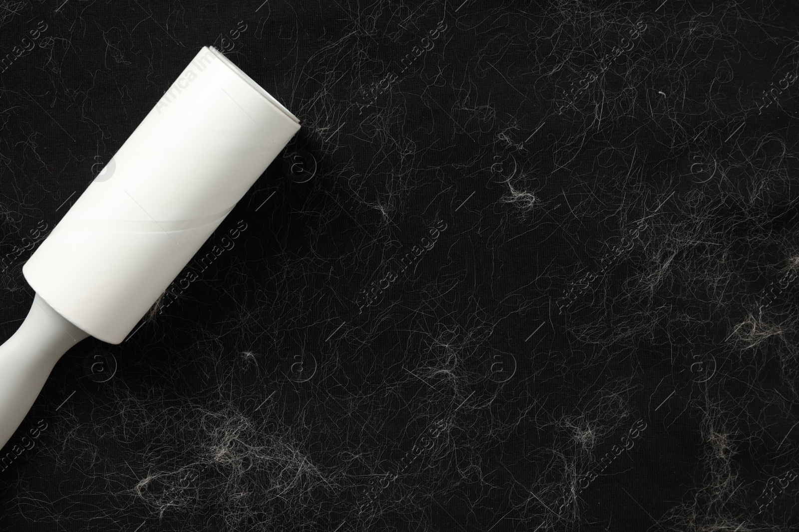 Photo of Lint roller and pet hair on black fabric, top view. Space for text