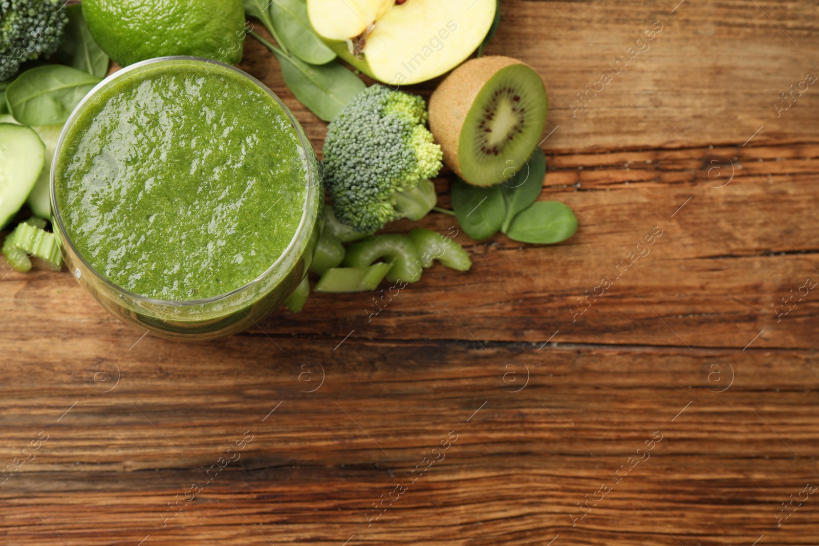 Photo of Green juice and fresh ingredients on wooden table, flat lay. Space for text