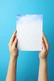 Photo of Woman holding blank invitation card on light blue background, closeup. Space for text