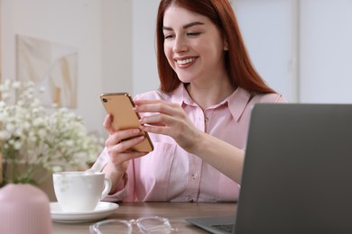 Photo of Beautiful woman with smartphone and laptop at wooden table in room