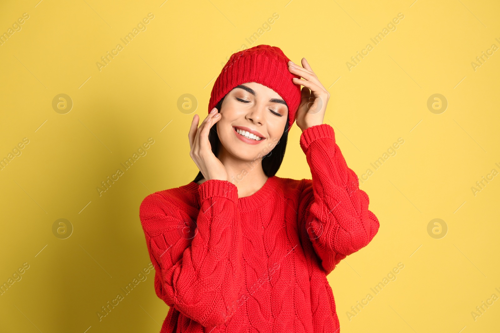 Photo of Young woman wearing warm sweater and hat on yellow background. Winter season