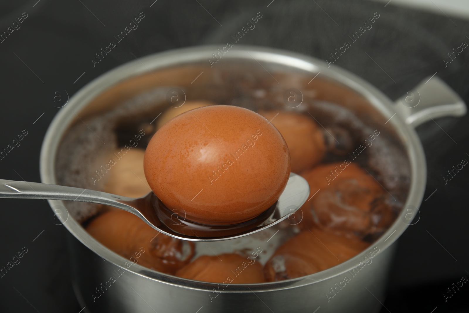 Photo of Spoon with boiled egg above saucepan on electric stove, closeup