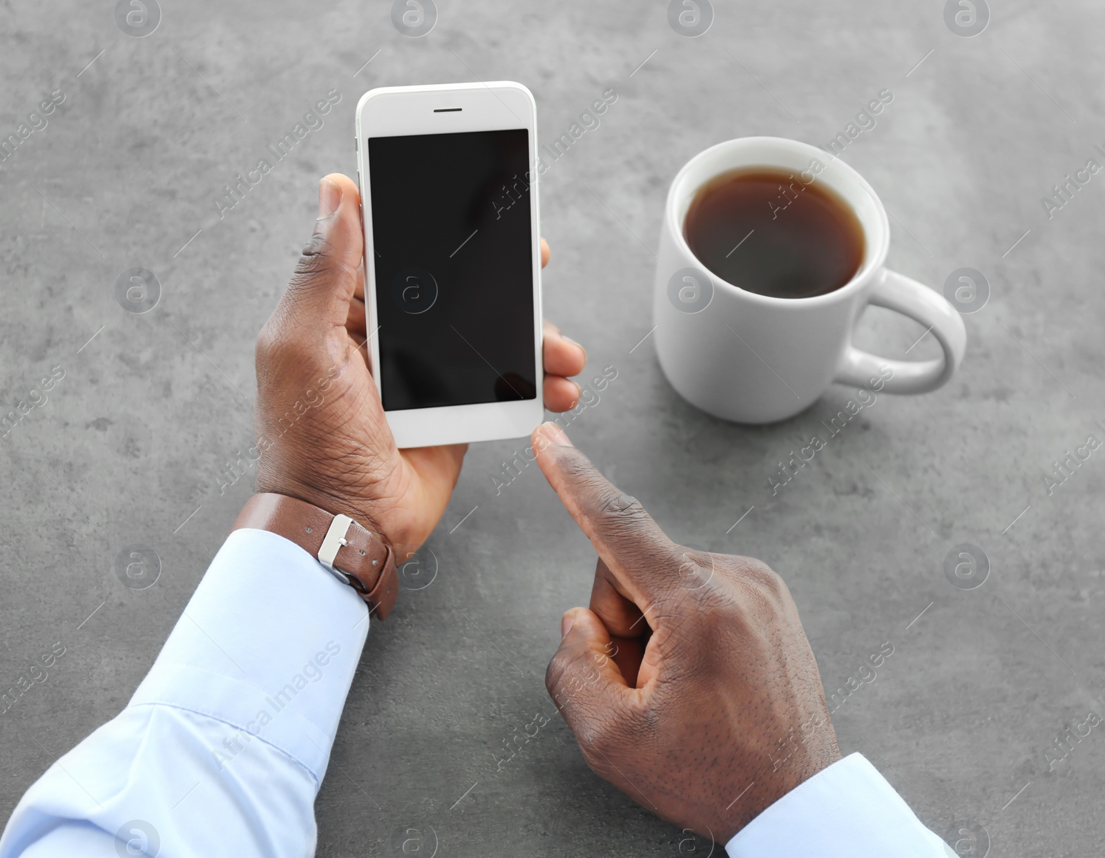 Photo of African-American man holding mobile phone with blank screen in hand at table