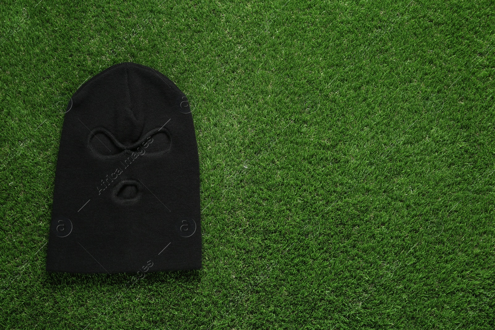 Photo of Black knitted balaclava on green grass, top view. Space for text