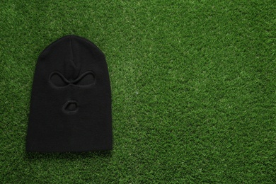 Photo of Black knitted balaclava on green grass, top view. Space for text