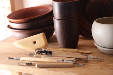 Set of different crafting tools and clay dishes on wooden table in workshop