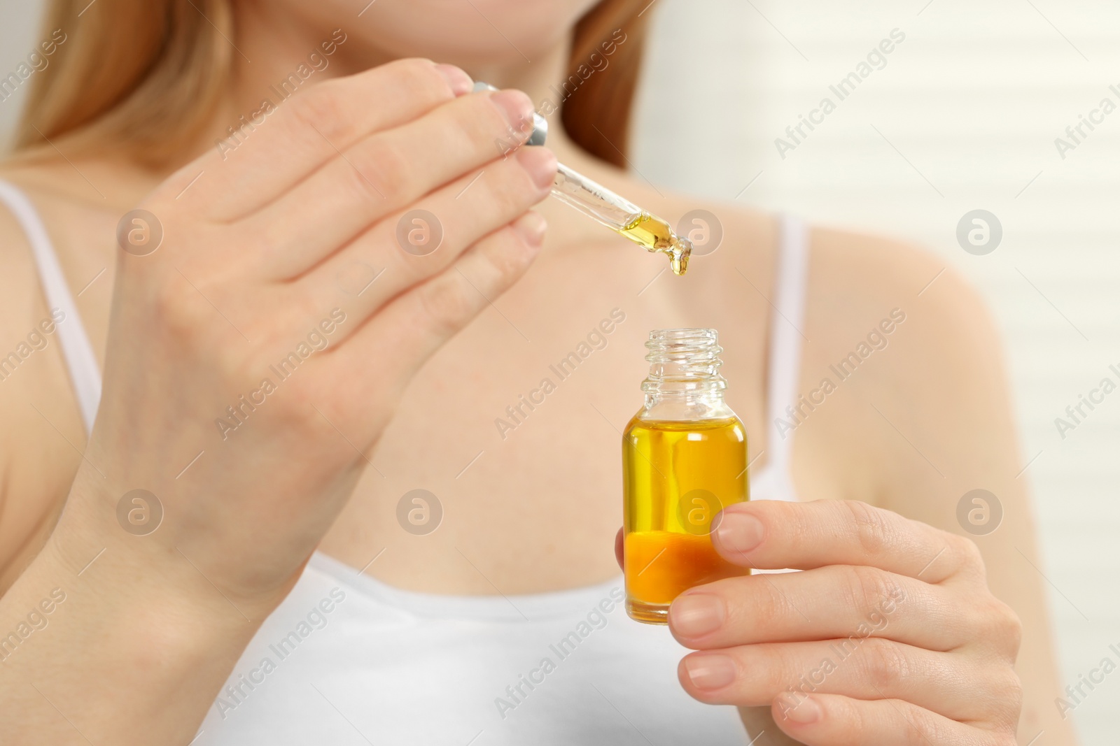 Photo of Woman with bottle of essential oil on blurred background, closeup