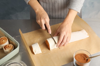 Woman cutting dough for cinnamon rolls on parchment at table, closeup