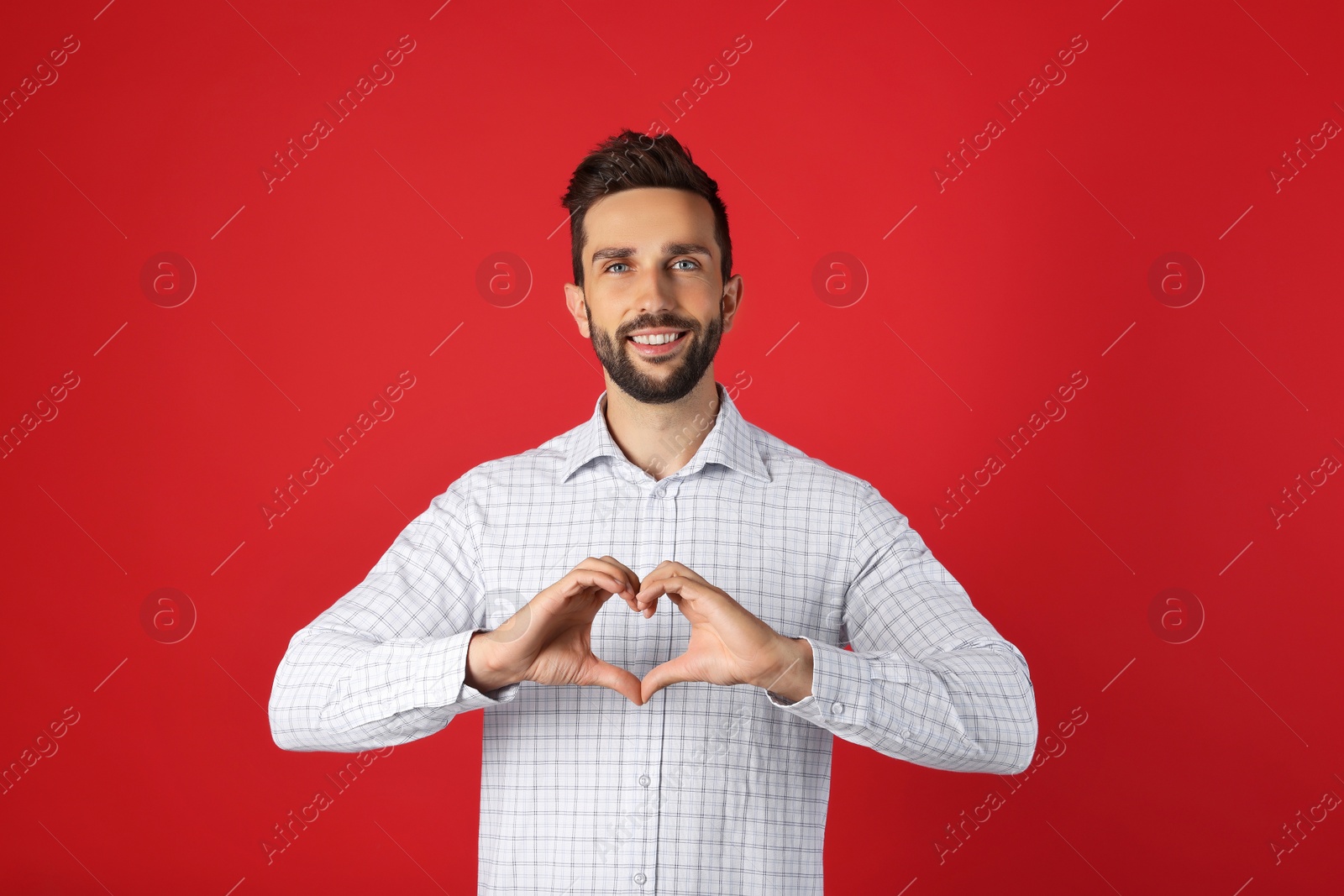 Photo of Happy man making heart with hands on red background