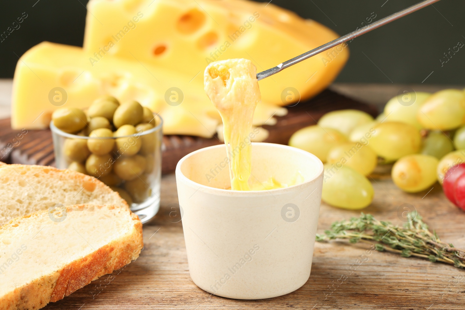 Photo of Piece of bread over bowl with delicious cheese fondue on wooden table