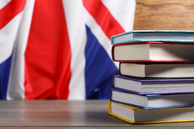 Learning foreign language. Different books on wooden table near flag of United Kingdom, space for text