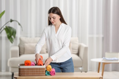 Photo of Young woman putting rolled shirt into basket at table in room. Organizing clothes