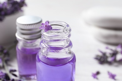 Glass bottles of natural cosmetic oil and lavender flowers on table, closeup