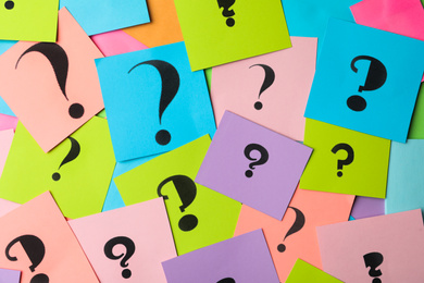 Different colorful paper cards with question marks as background, top view